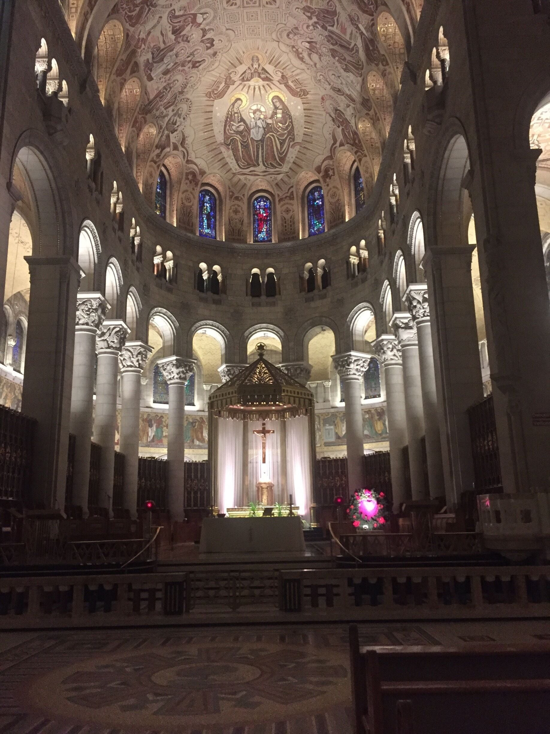 An ornate church interior with a central altar, high vaulted ceilings, and stained glass windows.