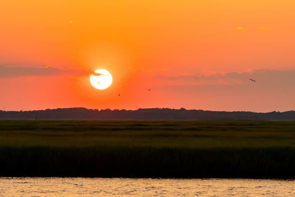 A sunset over a flat landscape with a body of water in the foreground.