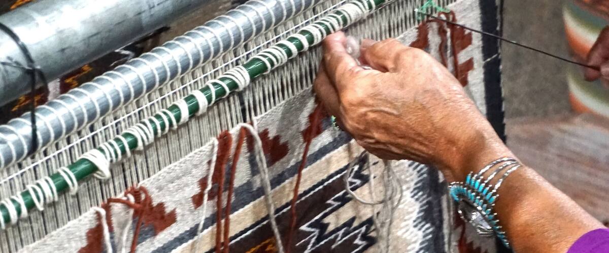 Cameron, Arizona: A Navajo woman demonstrates traditional rug weaving at the Cameron Trading Post,  a Native American cultural center.