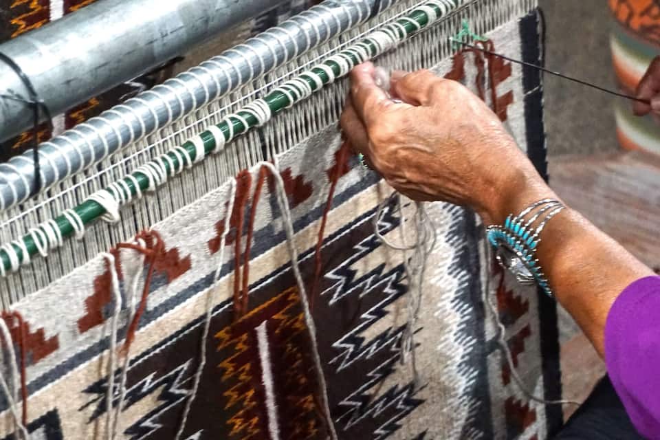 A person weaving a patterned textile with a traditional loom.