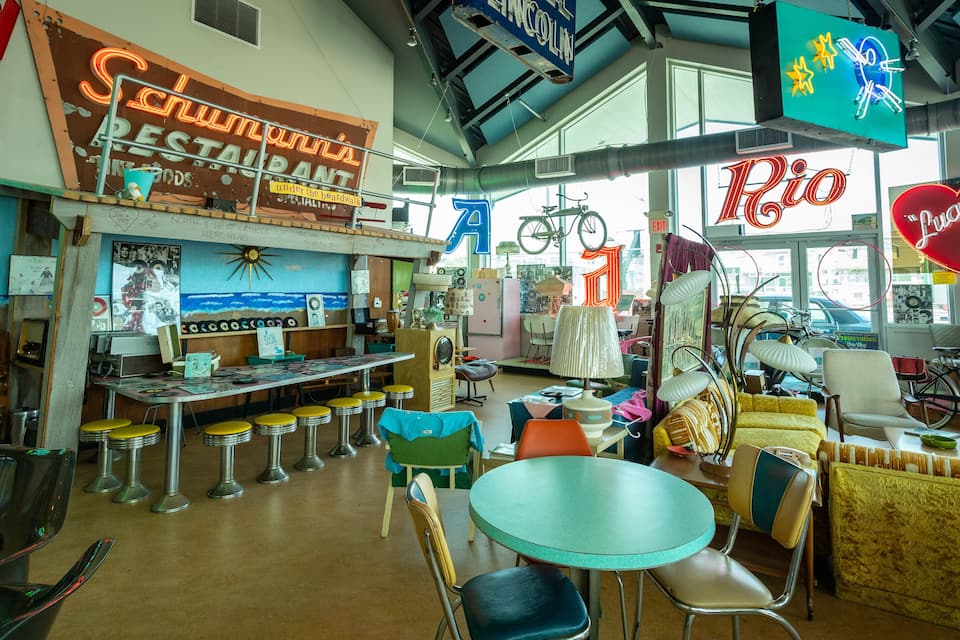 Interior de un restaurante de estilo retro con letreros de neón, muebles antiguos y una bicicleta.
