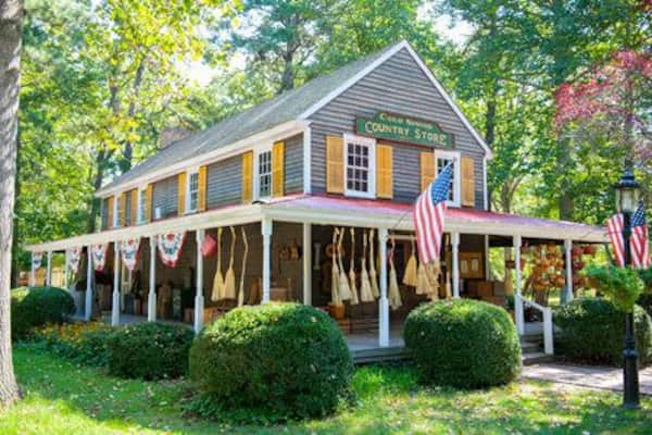 Uma loja de produtos rurais com varanda, bandeiras americanas e um letreiro que diz 'Country Store'.