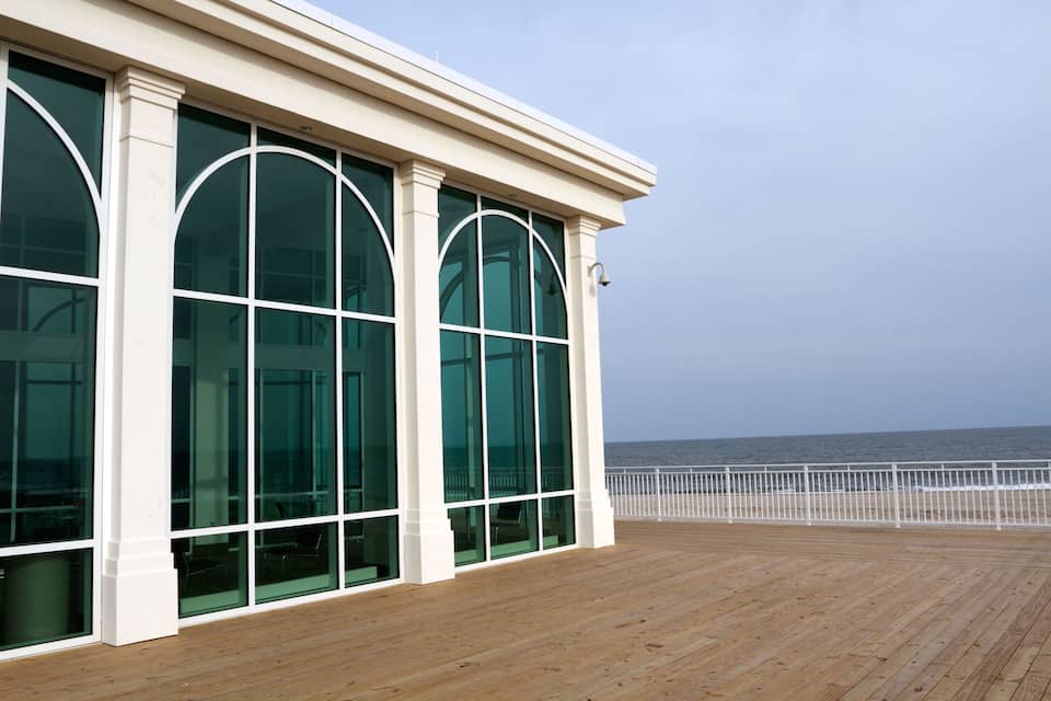 Een houten terras met grote glasramen met uitzicht op de oceaan.
