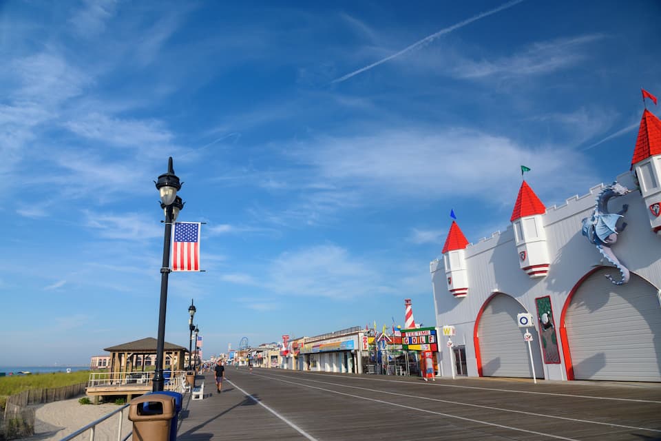 Um calçadão com um edifício que se assemelha a um castelo, bandeiras americanas e uma praia ao fundo.