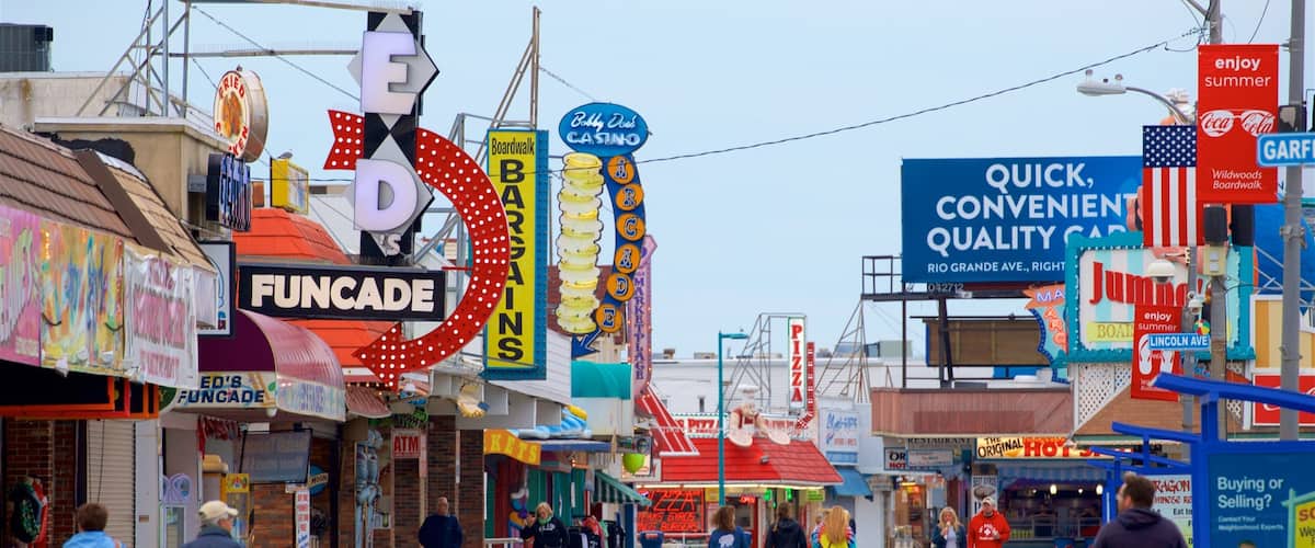 Paseo recreativo Wildwood Boardwalk ofreciendo escenas urbanas y señalización y también un pequeño grupo de personas