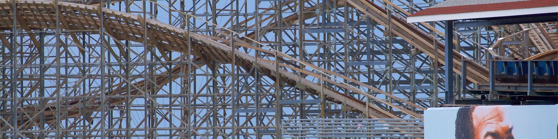 A roller coaster with a wooden structure and metal supports, a sign reading "Helicopter Rides", and a clear blue sky in the background.