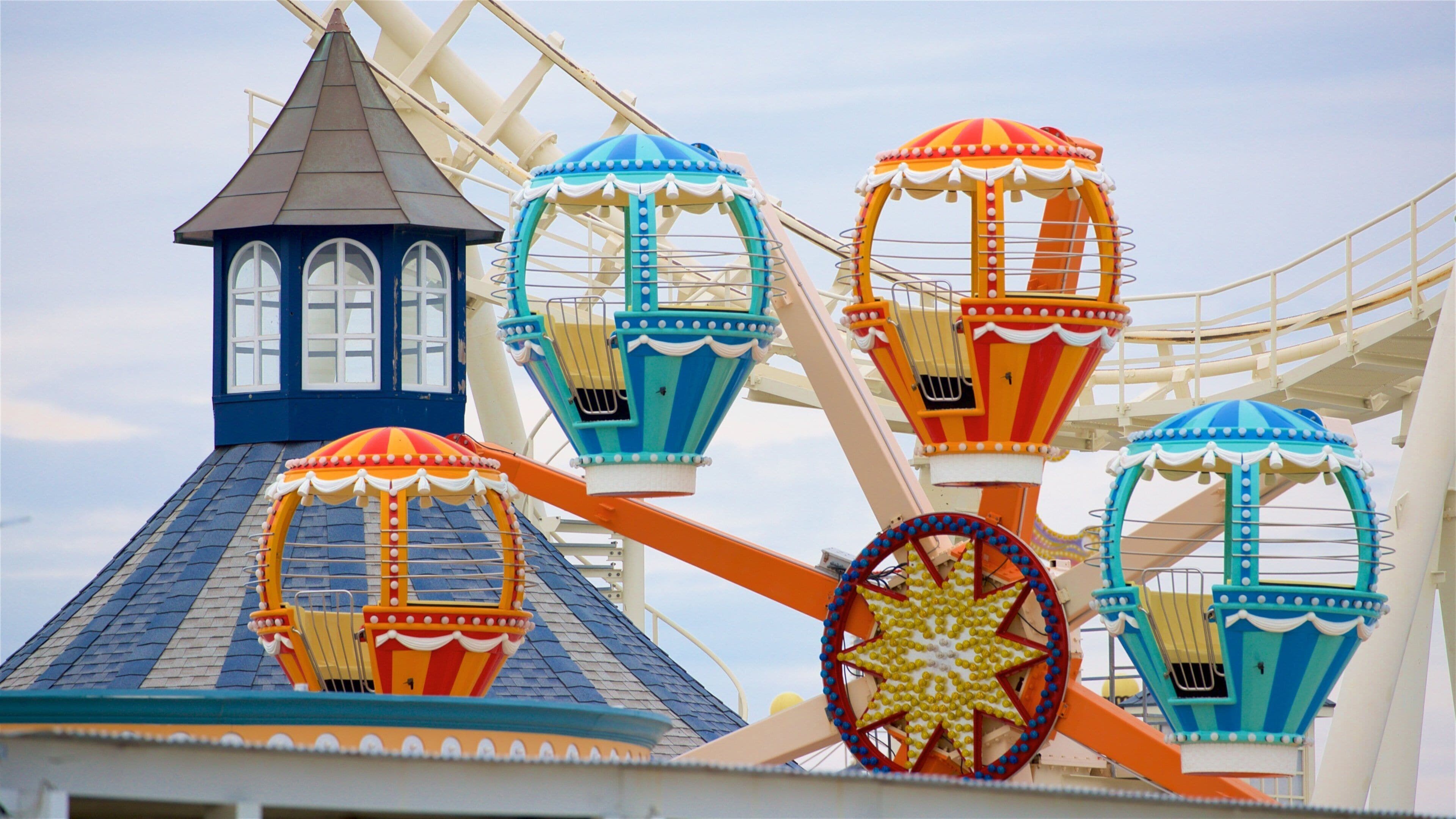 A Ferris wheel with colorful gondolas and a building with a pointed roof.