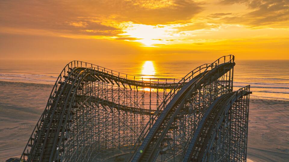 A roller coaster at sunset with the sun setting over the ocean.
