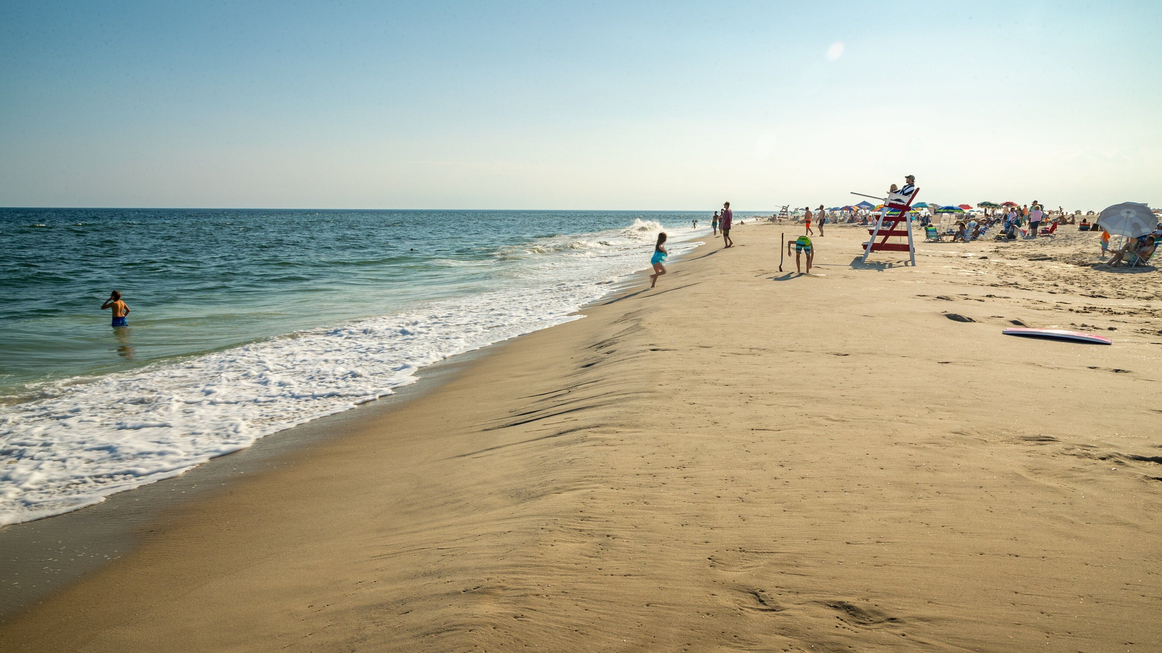 A sandy beach with people walking and swimming.