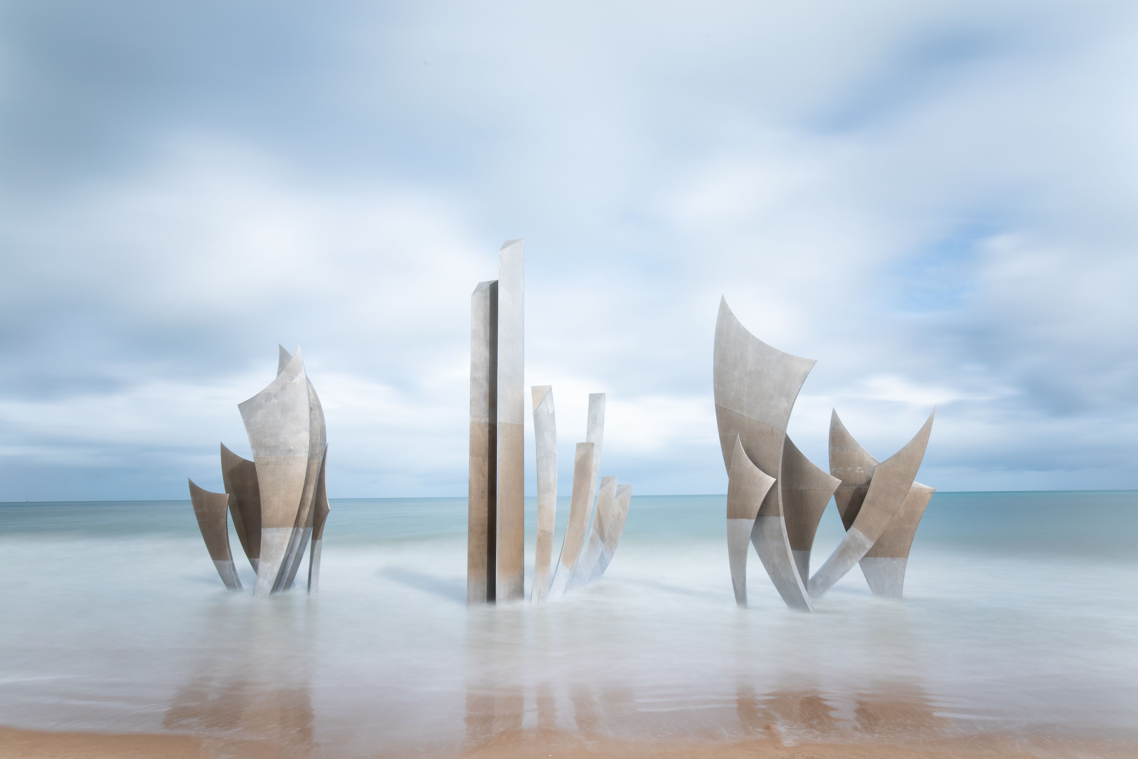 Abstract sculptures on a beach with the ocean in the background.