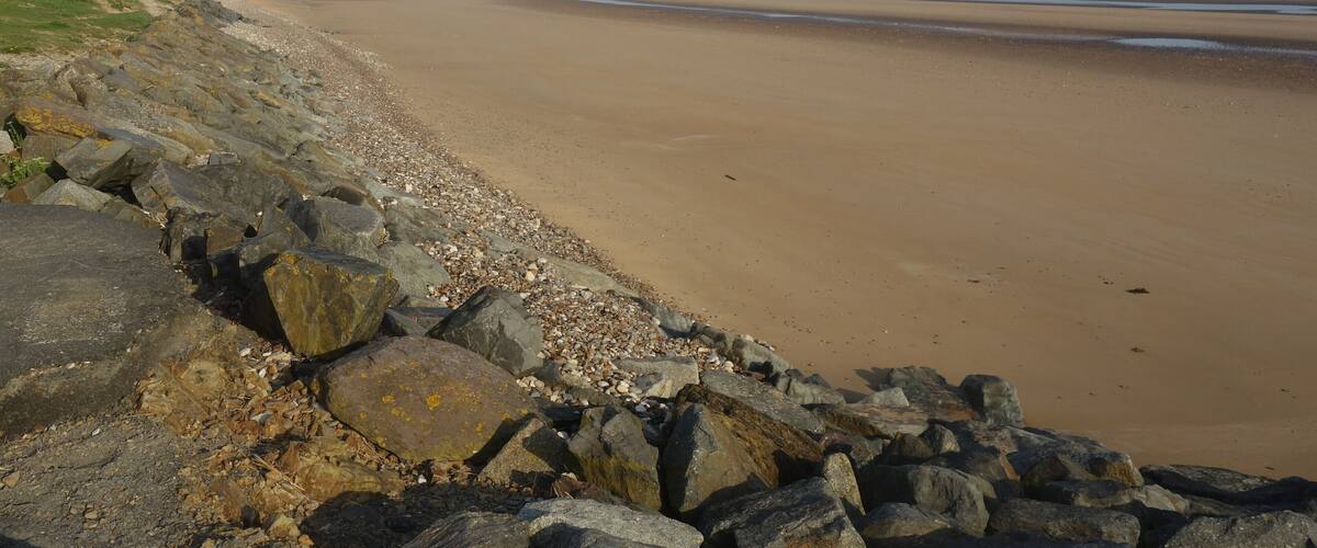 A wide sandy beach with a rocky shoreline and distant hills.