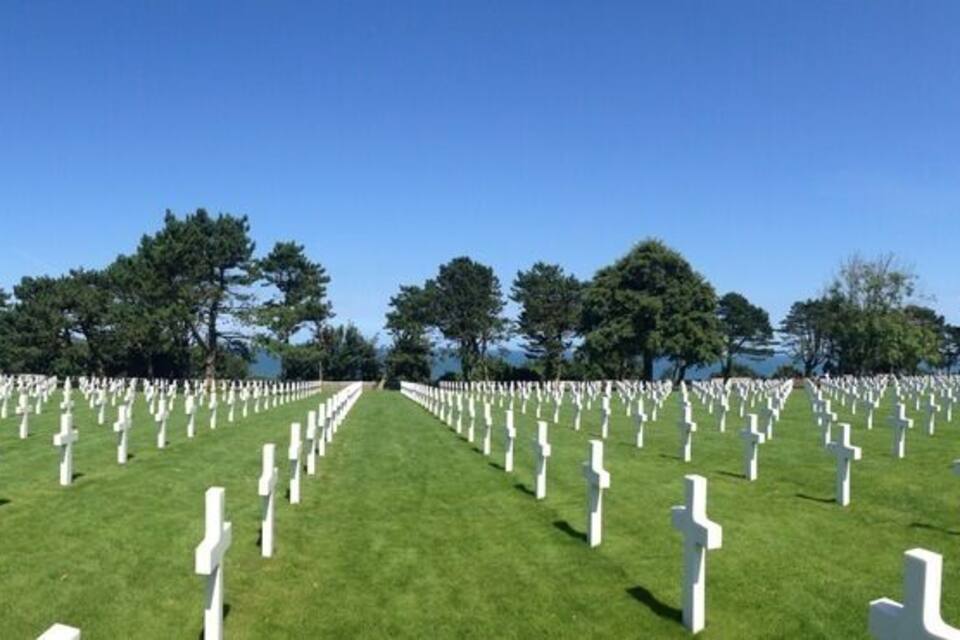 A cemetery with rows of white crosses on green grass under a clear blue sky.