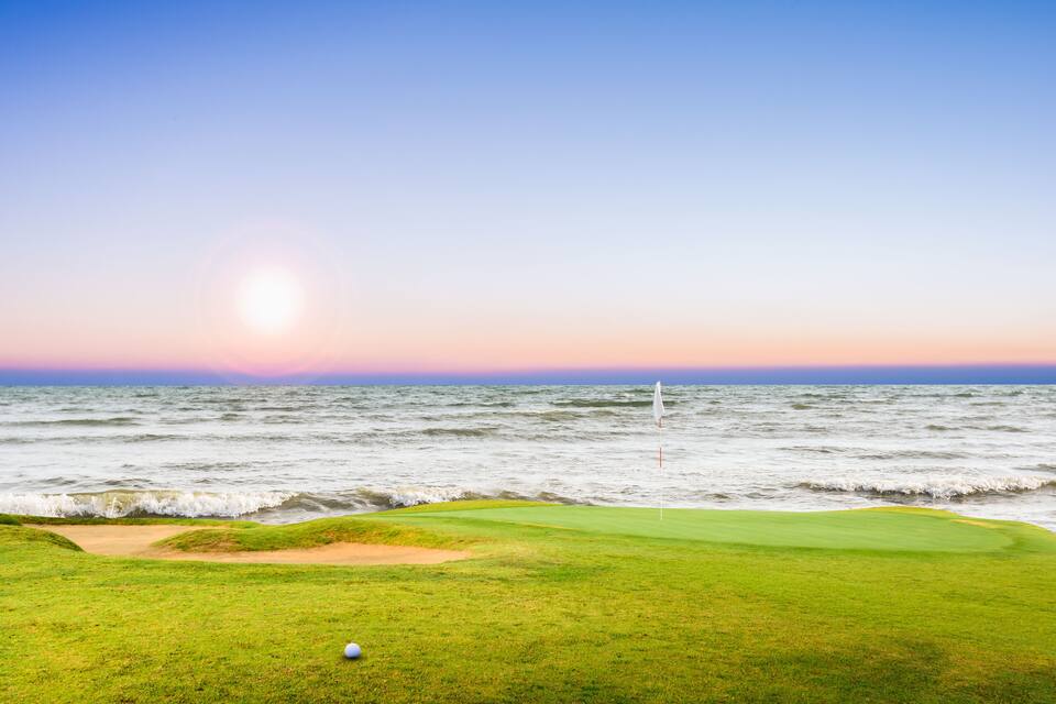 Camp de golf amb un forat cap a l'oceà al capvespre.