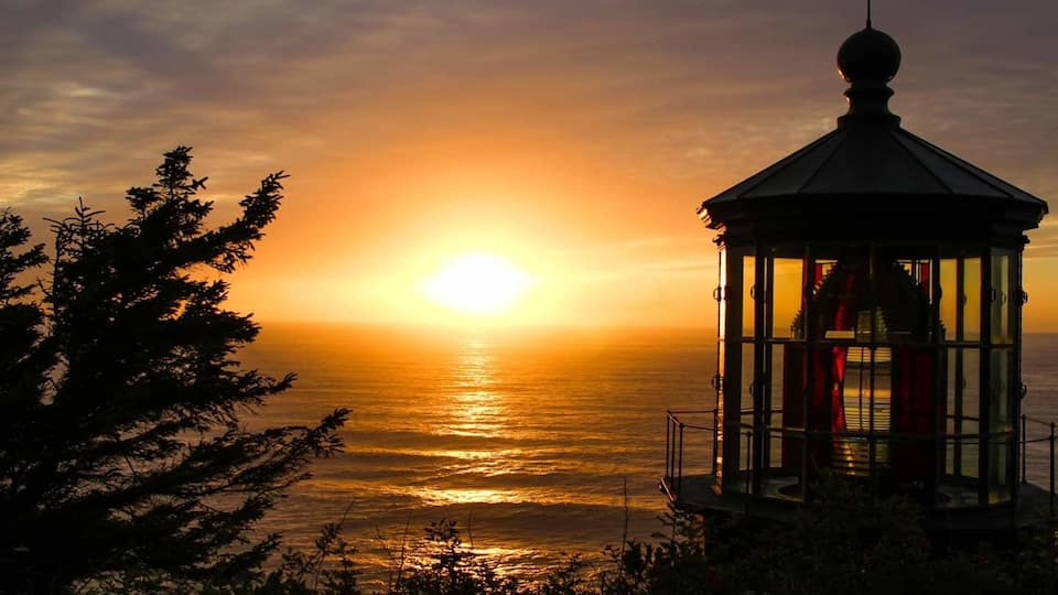 A sunset over the ocean with a lighthouse in the foreground.