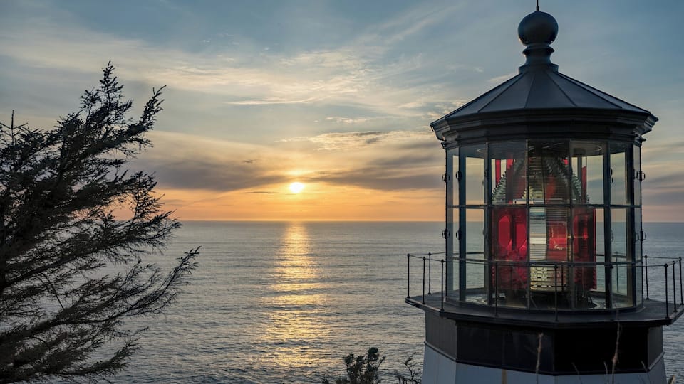 A lighthouse at sunset with the sun reflecting on the water.