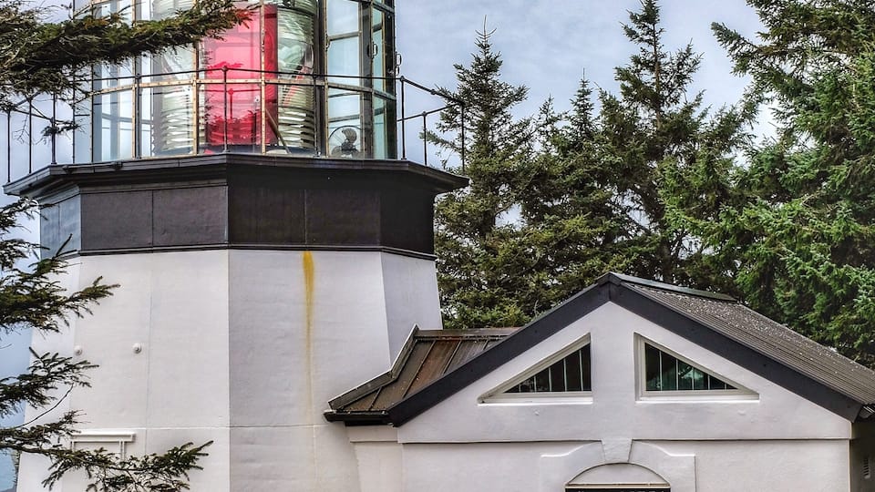 A lighthouse with a white exterior and a black top, surrounded by trees.