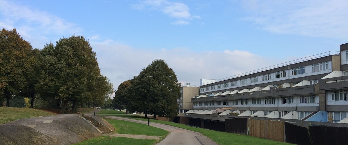 A pathway leading to a multi-story residential building with a modern design, surrounded by trees and grassy areas.