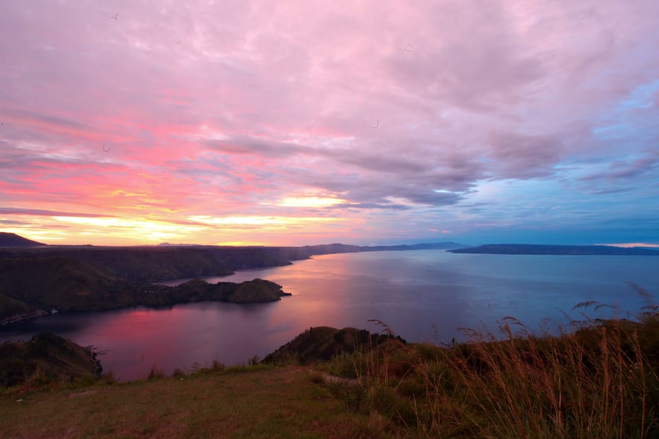 A sunset over a calm lake surrounded by hills.