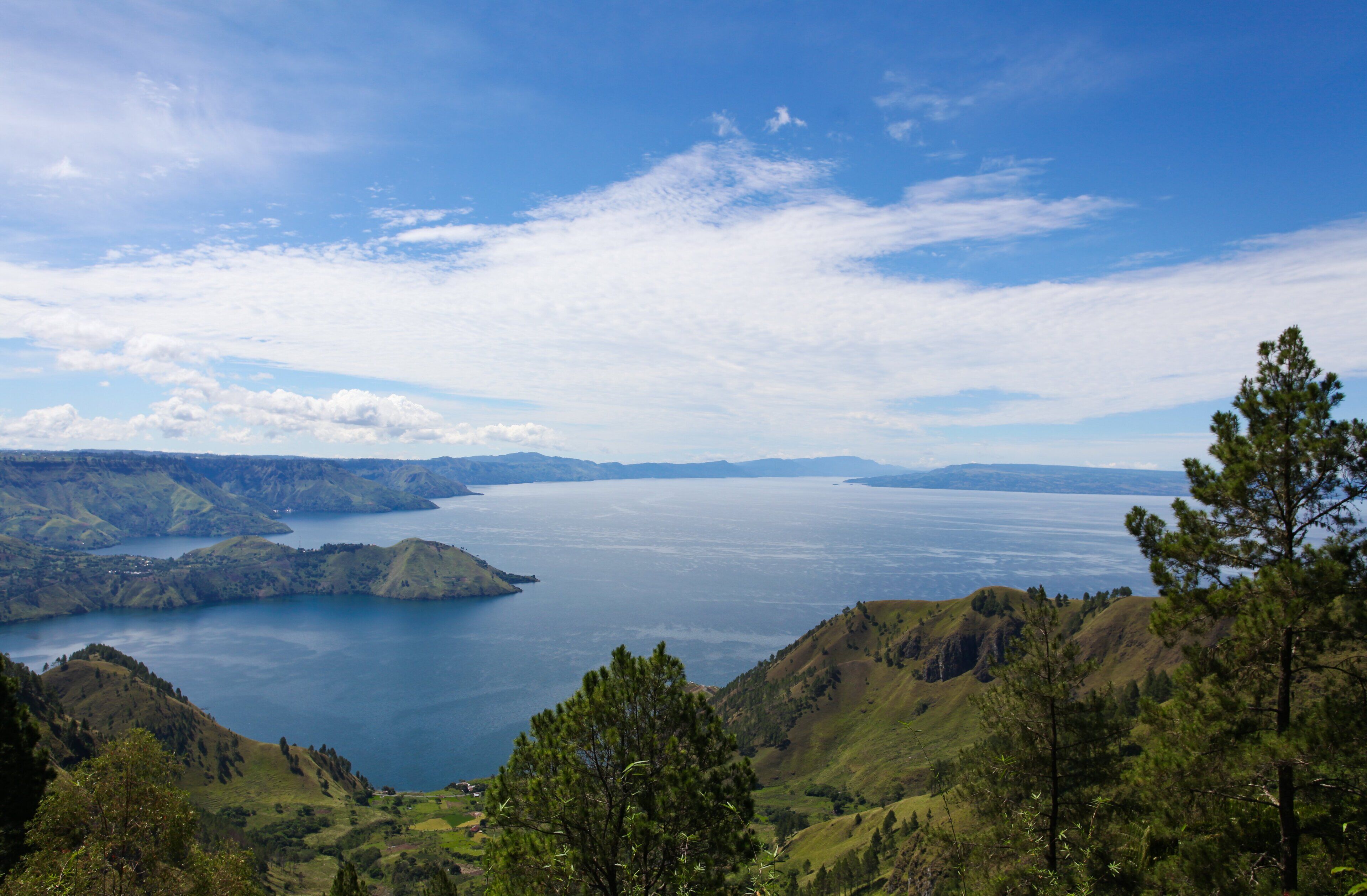 Une vue panoramique d’un grand lac, entouré de collines verdoyantes et de montagnes.