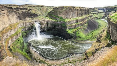 A waterfall cascading into a river surrounded by rugged cliffs and green vegetation.