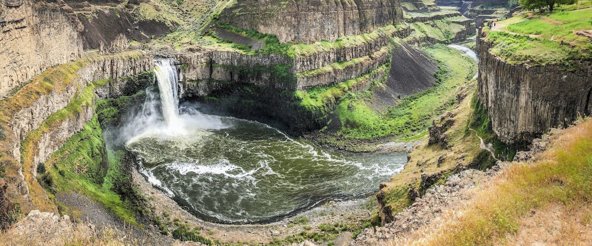A waterfall cascading into a river surrounded by rugged cliffs and green vegetation.