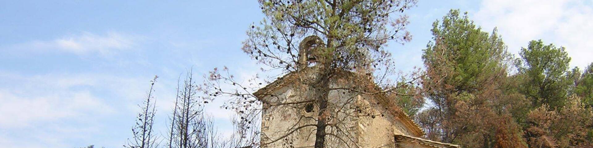 A stone chapel with a tree in front, surrounded by rocky terrain and sparse vegetation.