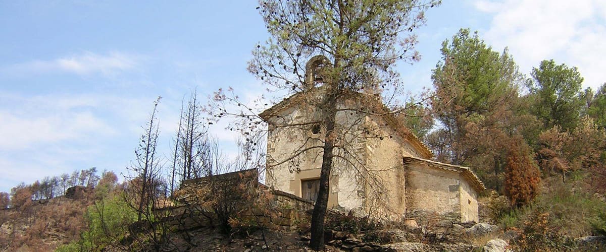A stone chapel with a tree in front, surrounded by rocky terrain and sparse vegetation.