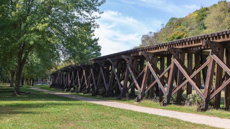 A wooden trestle bridge in a park with a path alongside it.