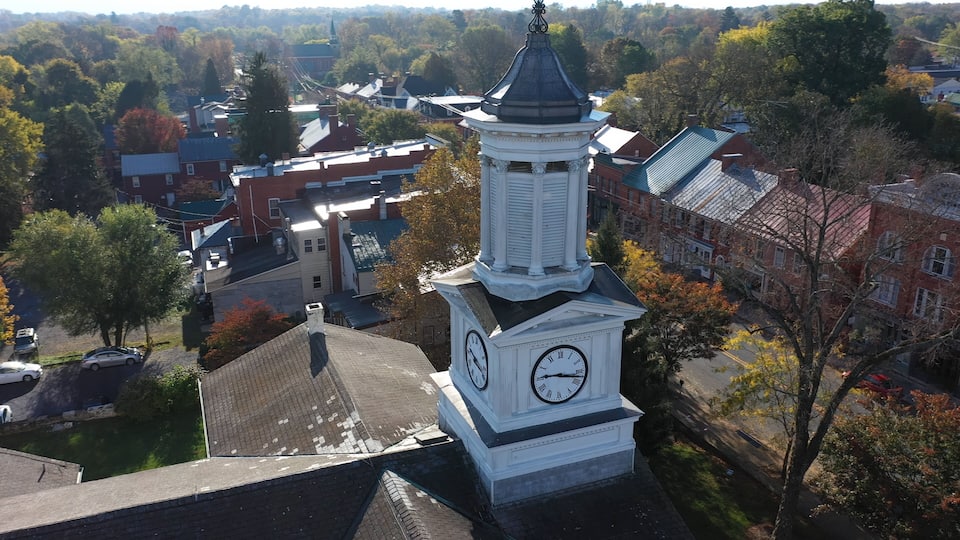 A clock tower with Roman numerals, surrounded by autumn-colored trees and buildings.
