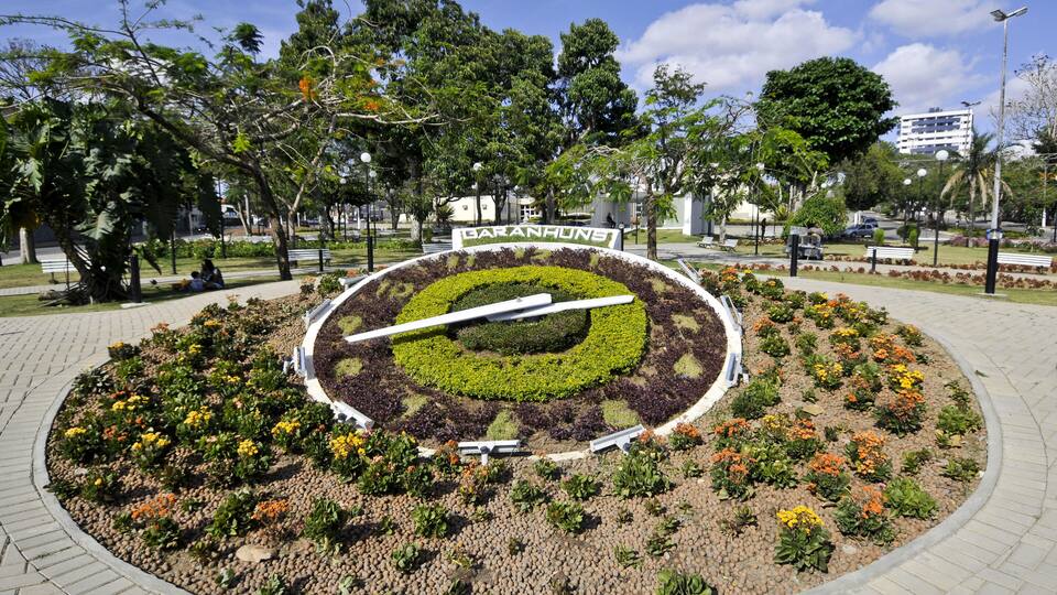 A circular garden with a central sculpture, surrounded by trees and benches.