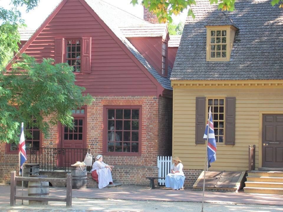 A historical reenactment scene with colonial-style buildings, flags, and costumed individuals.