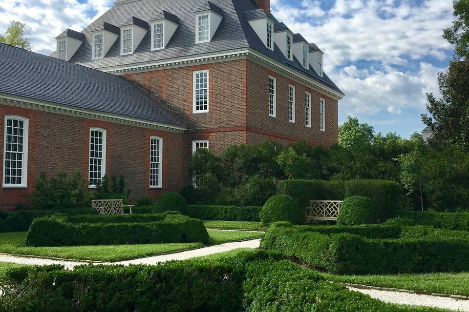 A large brick building with a tower and a garden with hedges and a pathway.