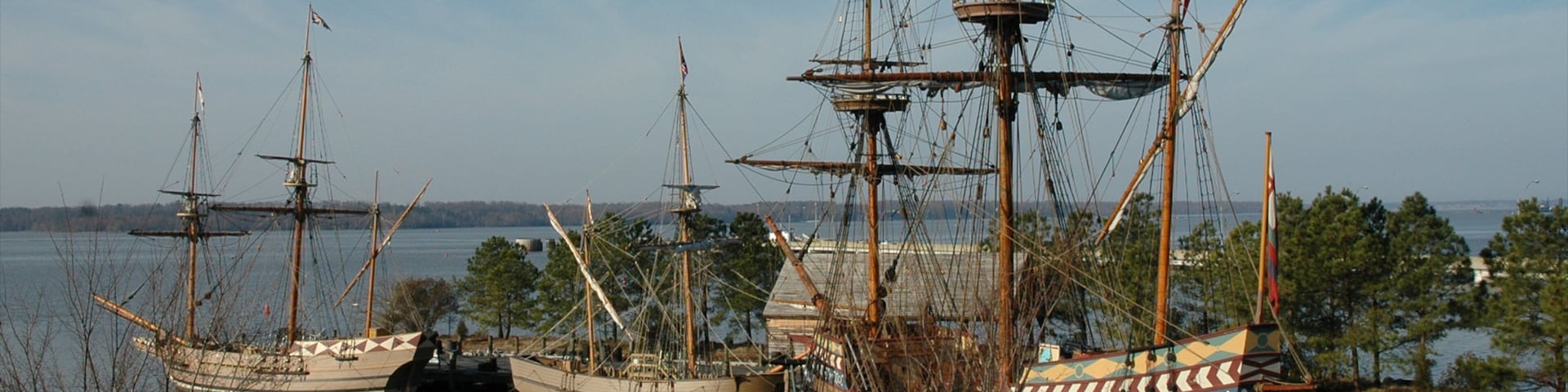 Tres barcos de vela históricos amarrados en un puerto con cielo despejado y aguas tranquilas.
