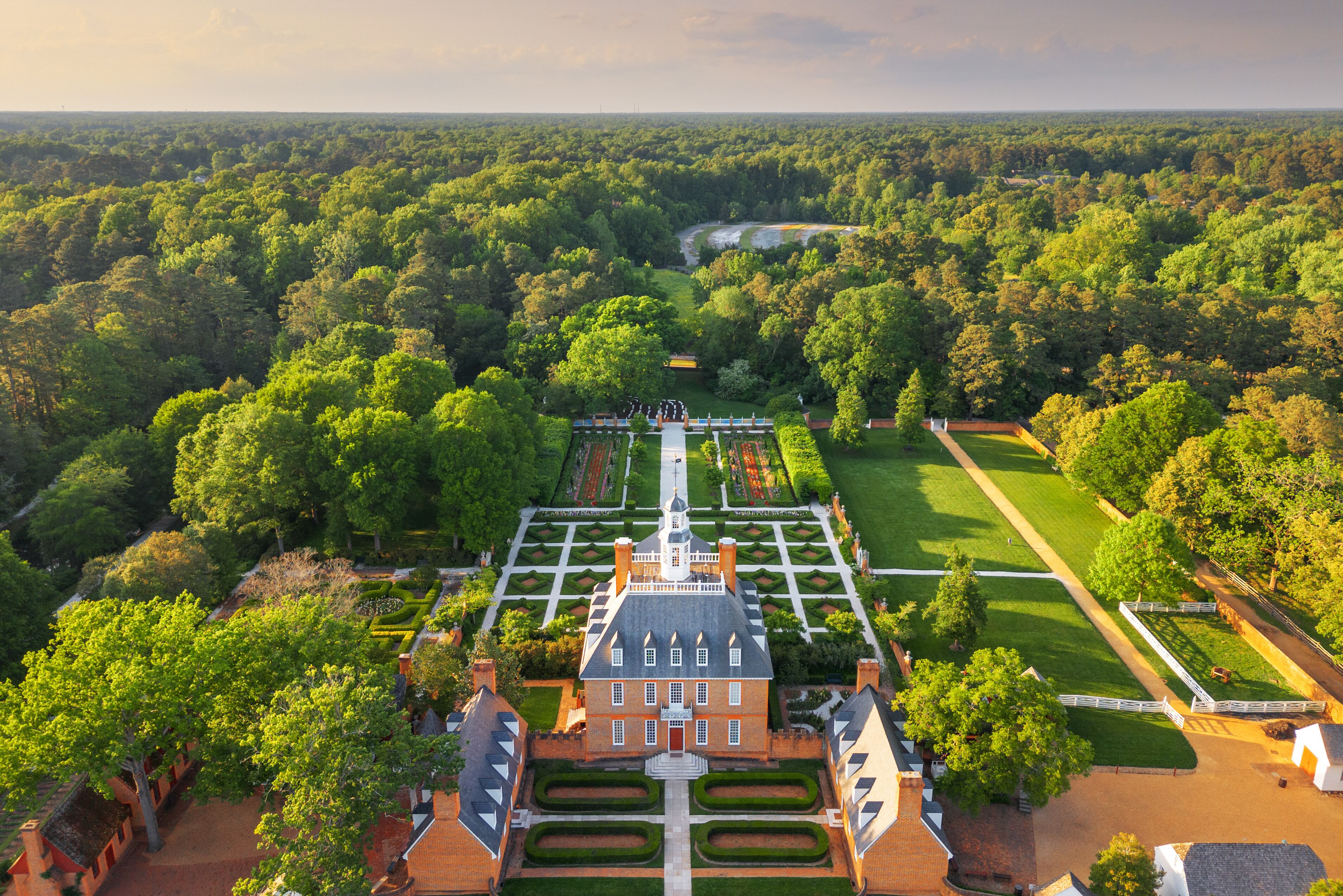 A large estate with a symmetrical garden, a central building with a tower, and a surrounding forest.
