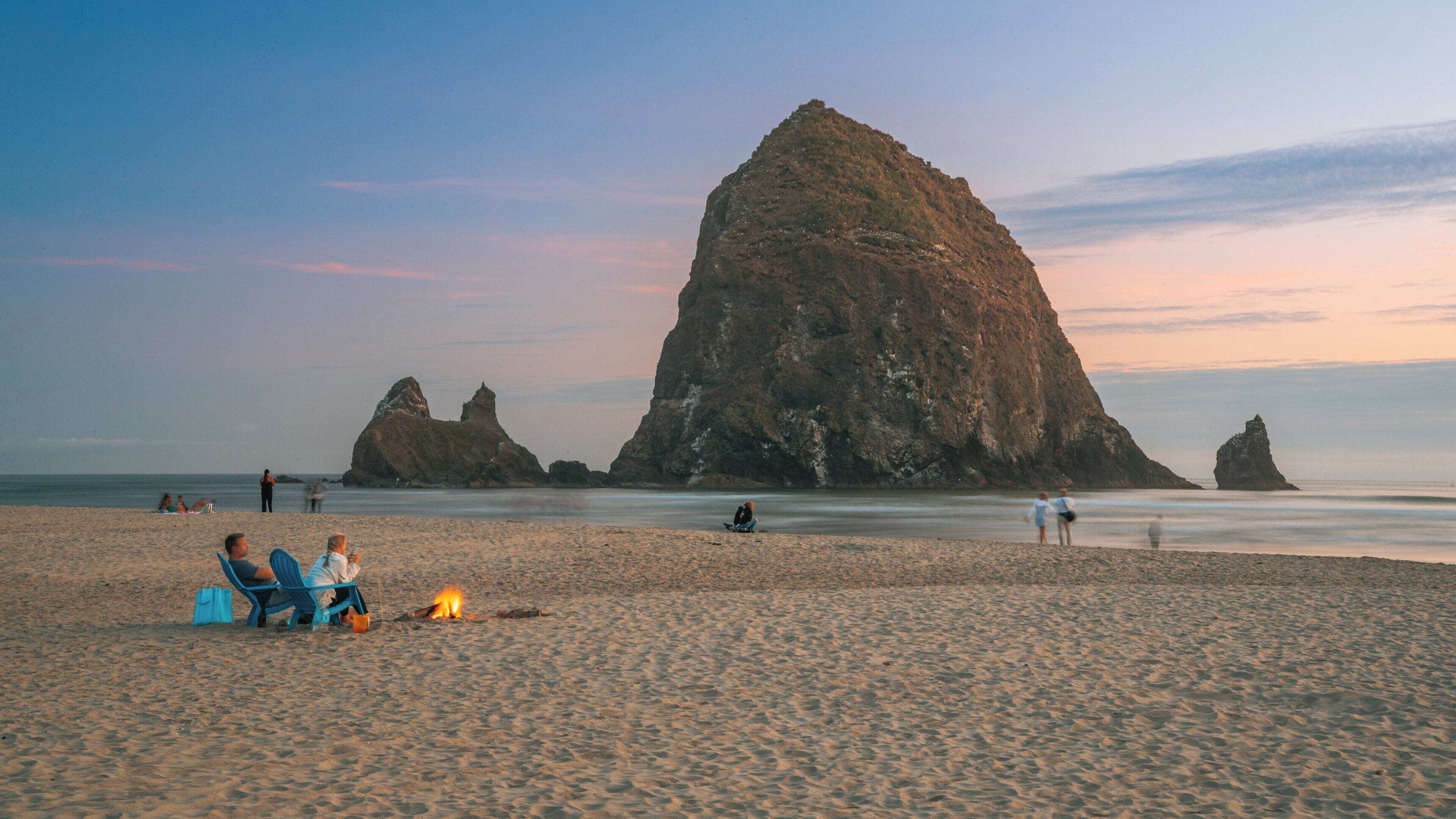 Sunset at Haystack Rock in Cannon Beach, Oregon, with friends enjoying a cozy fire on the sandy shore
