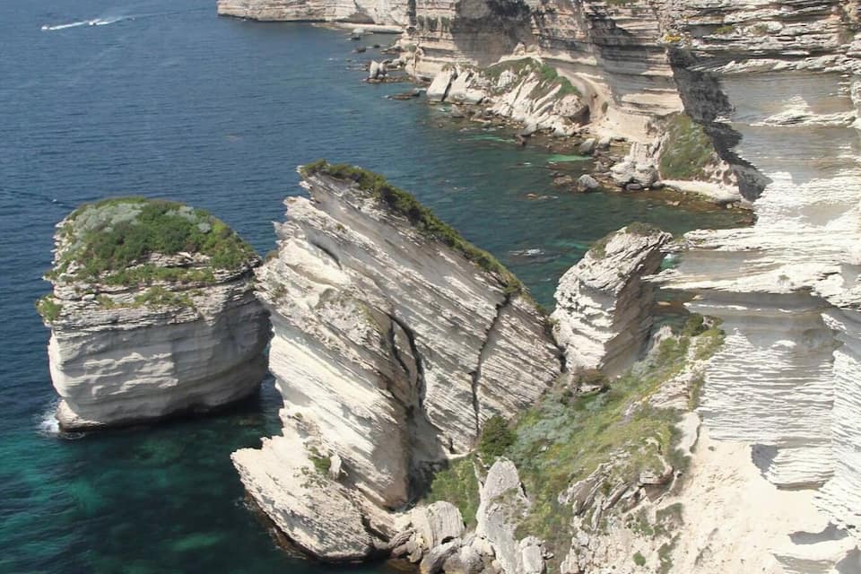 Une falaise côtière surplombant une eau d’un bleu limpide, avec des formations rocheuses et des bâtiments situés au sommet de la falaise.