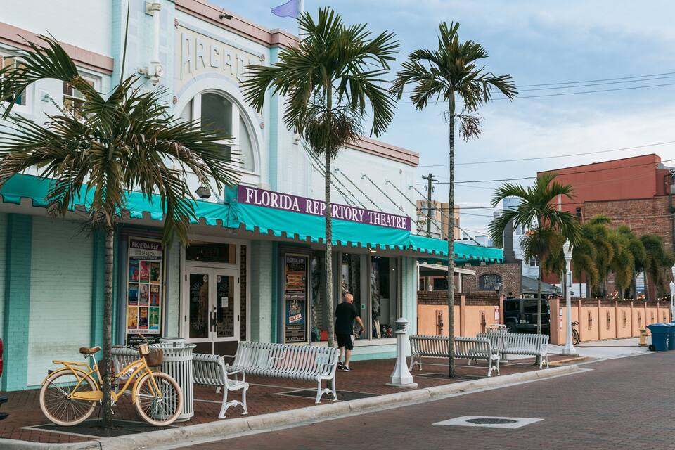 A Florida Repurtry Theatre with a teal awning, palm trees, and a parked bicycle.