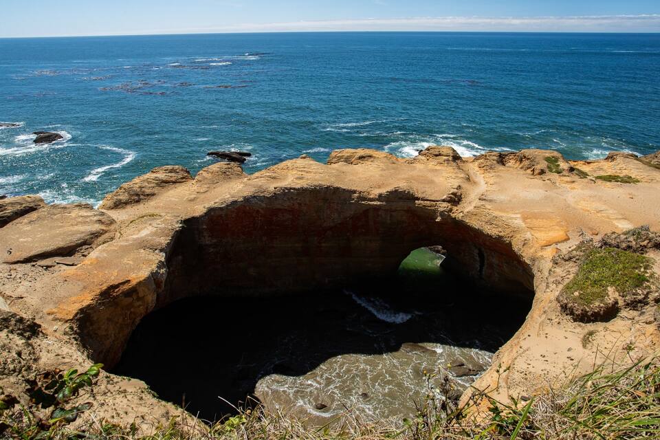 A coastal landscape with a large cave entrance, rocky shoreline, and the ocean in the background.