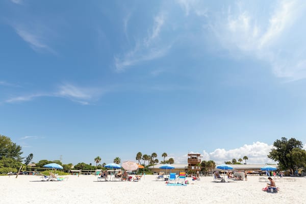Ein Strand mit Sonnenschirmen, Liegestühlen und Palmen.