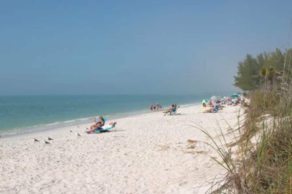 A sandy beach with people sunbathing and umbrellas, clear blue sky, and calm sea.