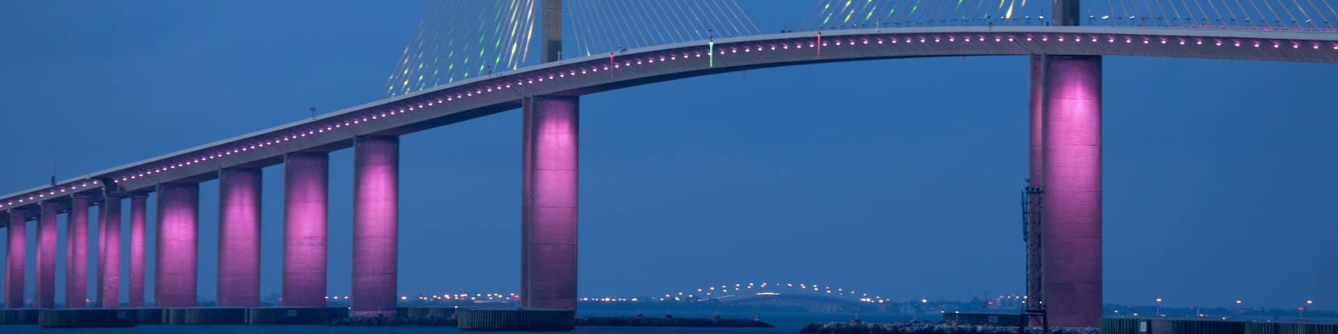 Closeup of the iconic Sunshine Skyway Bridge spanning the wide mouth of beautiful Tampa Bay in central Florida lit up in pink LED lights to commemorate Breast Cancer Awareness Month.