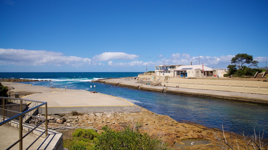 A coastal scene with a rocky shoreline, a pier, and a building with a white roof.
