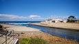 En kustvy med en stenig strand, en pir och en byggnad med ett vitt tak.