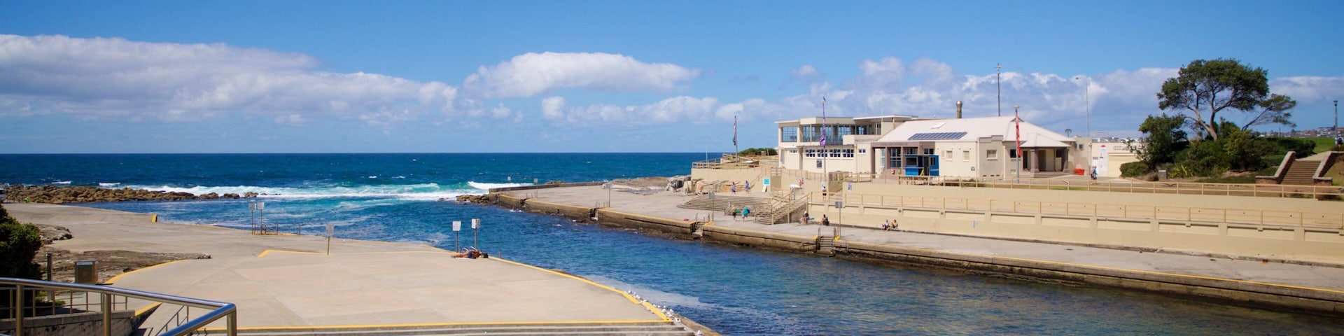 A coastal scene with a rocky shoreline, a pier, and a building with a white roof.