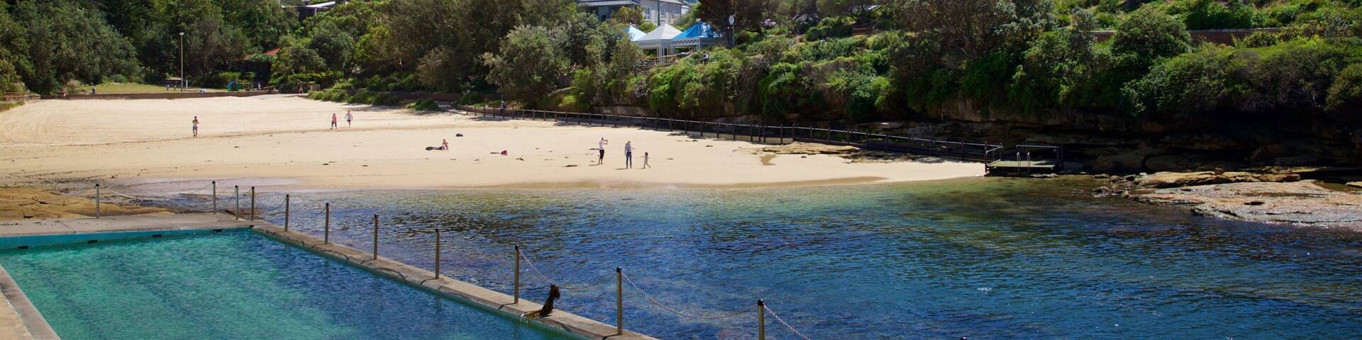 A swimming pool, a sandy beach, and houses in the background.