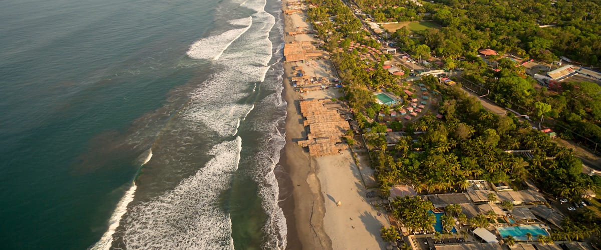 An aerial view of a coastal area with a beach, a river, and a residential area with houses and greenery.