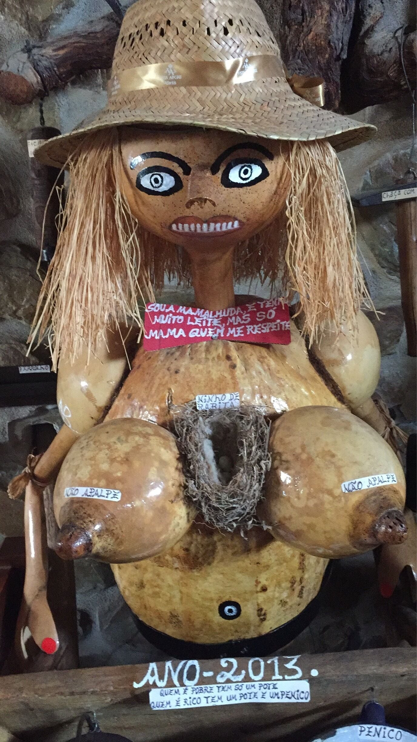A sculpture with a straw hat, a red ribbon, and a label reading "Ano 2013".