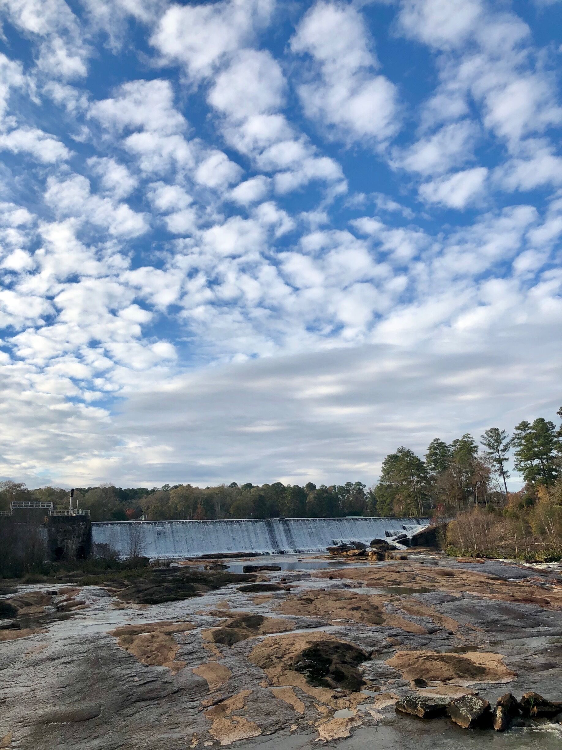 A dam with a waterfall, rocky terrain, and a forest in the background.