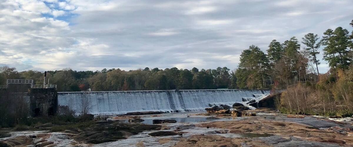 A dam with a waterfall, rocky terrain, and a forest in the background.