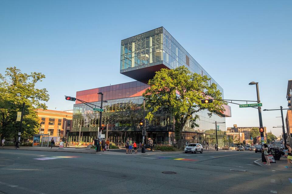 Een modern gebouw met een glazen gevel en een rood dak op een kruising.